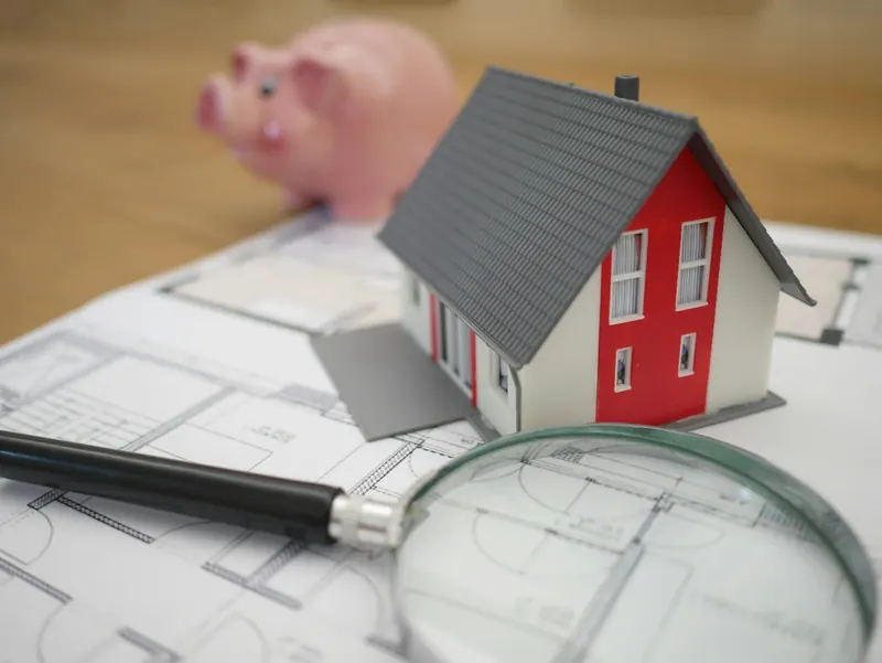 Cofrinho sobre planta de casa com miniatura de imóvel